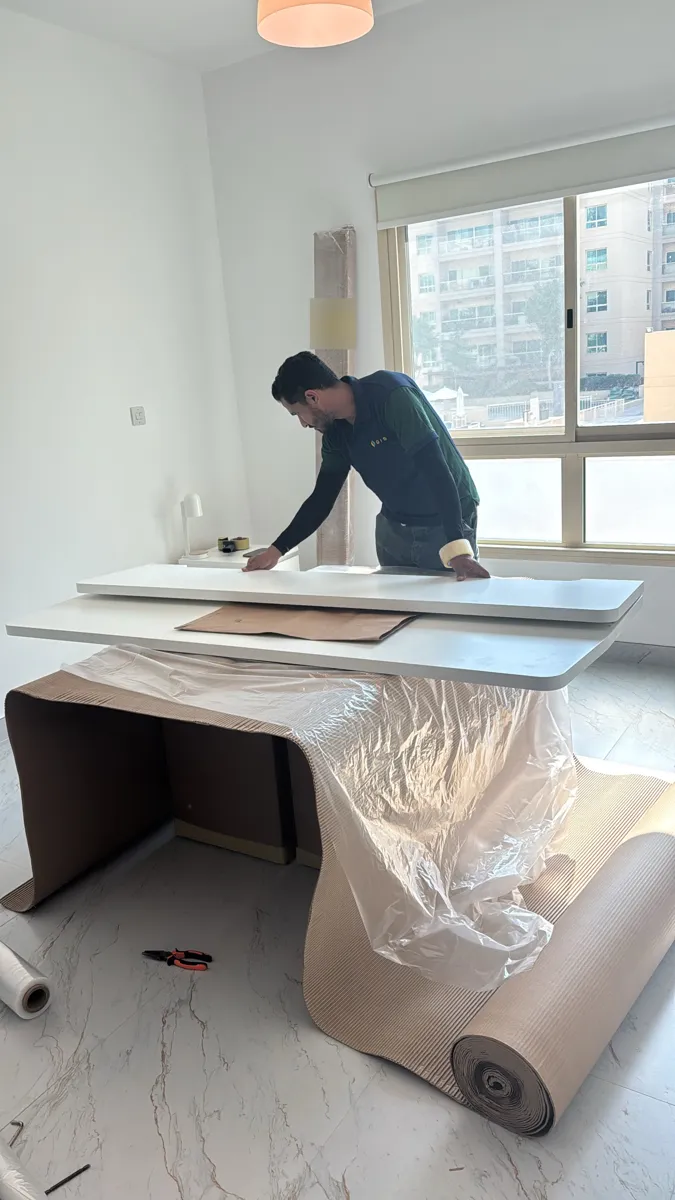 GPS Movers crew protecting a white tabletop with corrugated sheet and plastic