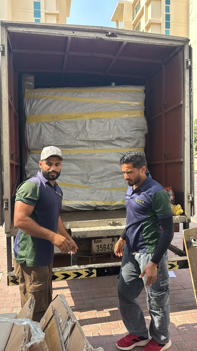 Two GPS Movers crew members beside a closed box truck with a wrapped mattress loaded inside