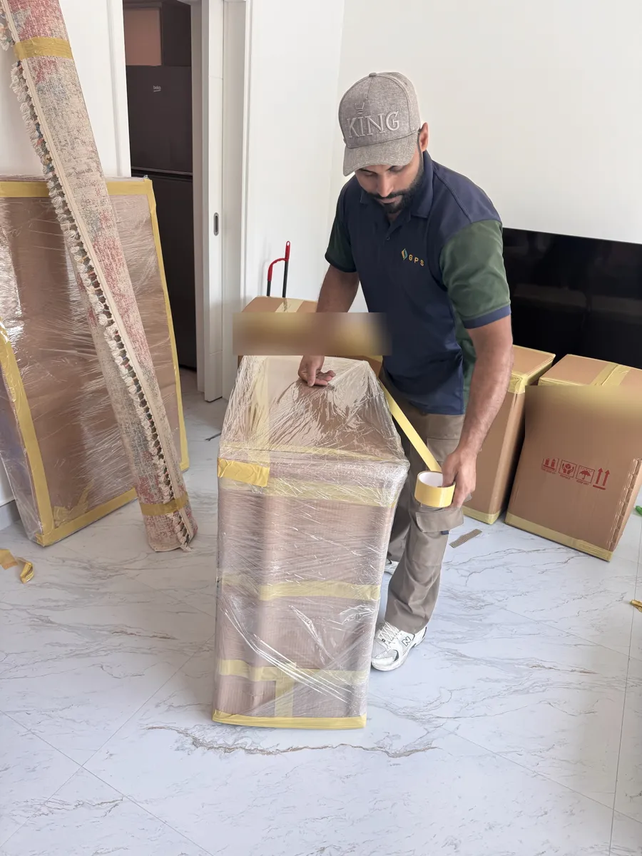 GPS Movers crew member taping stretch-wrapped furniture in a Dubai apartment